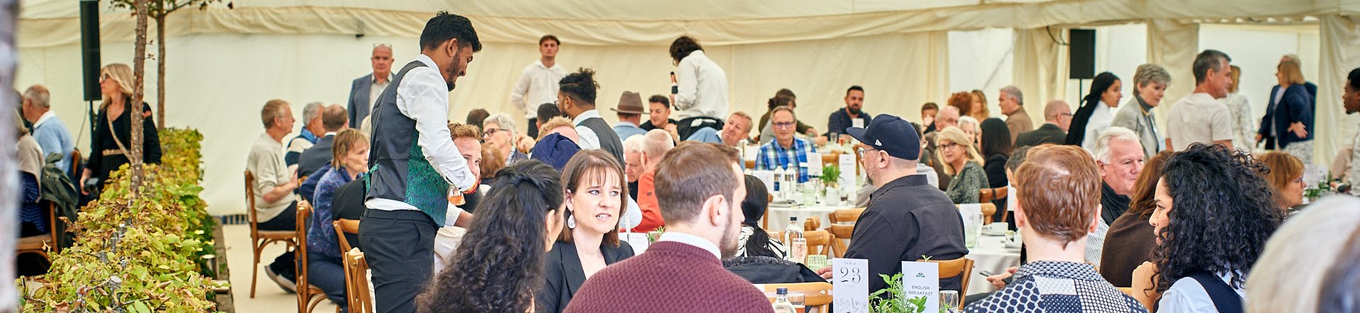 Elegant outdoor dining event under a marquee Guests enjoying a meal at round tables in a large tent