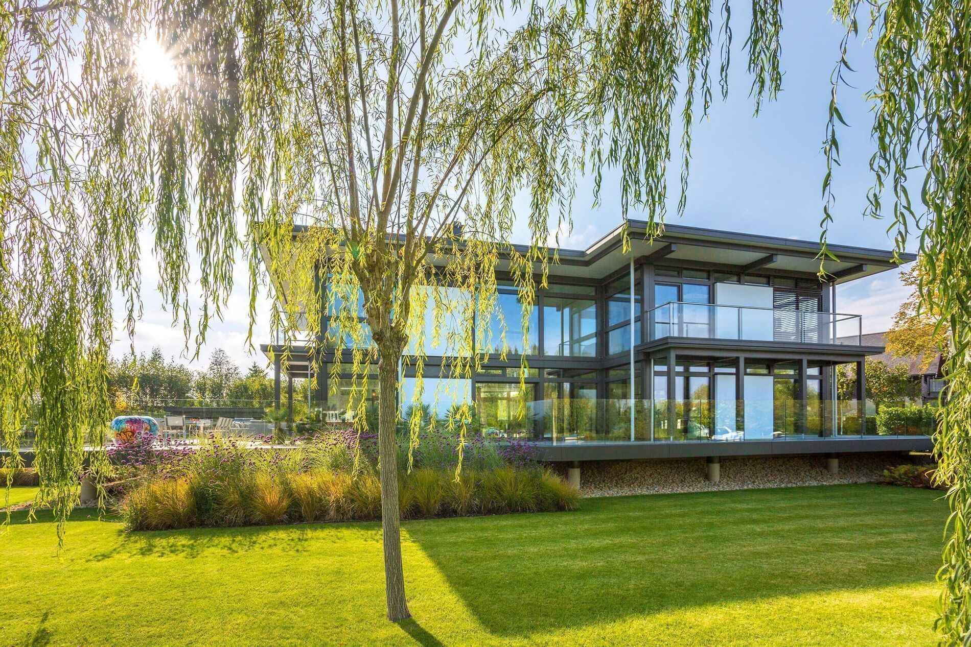 Luxushaus mit Flachdach in sonniger Gartenlandschaft Modernes Flachdachhaus umgeben von grünem Rasen und Weidenbaum