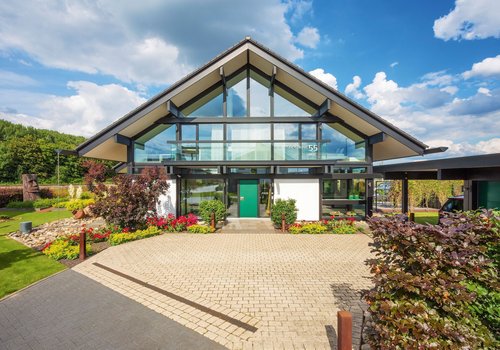 Moderne Architektur mit Glasfront und Garten Helles Gebäude mit Glasfront, umgeben von Blumen und Grünflächen.