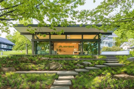 Modernes HUF Haus in grüner Umgebung HUF Haus mit Glasfront, umgeben von Bäumen und Steinen